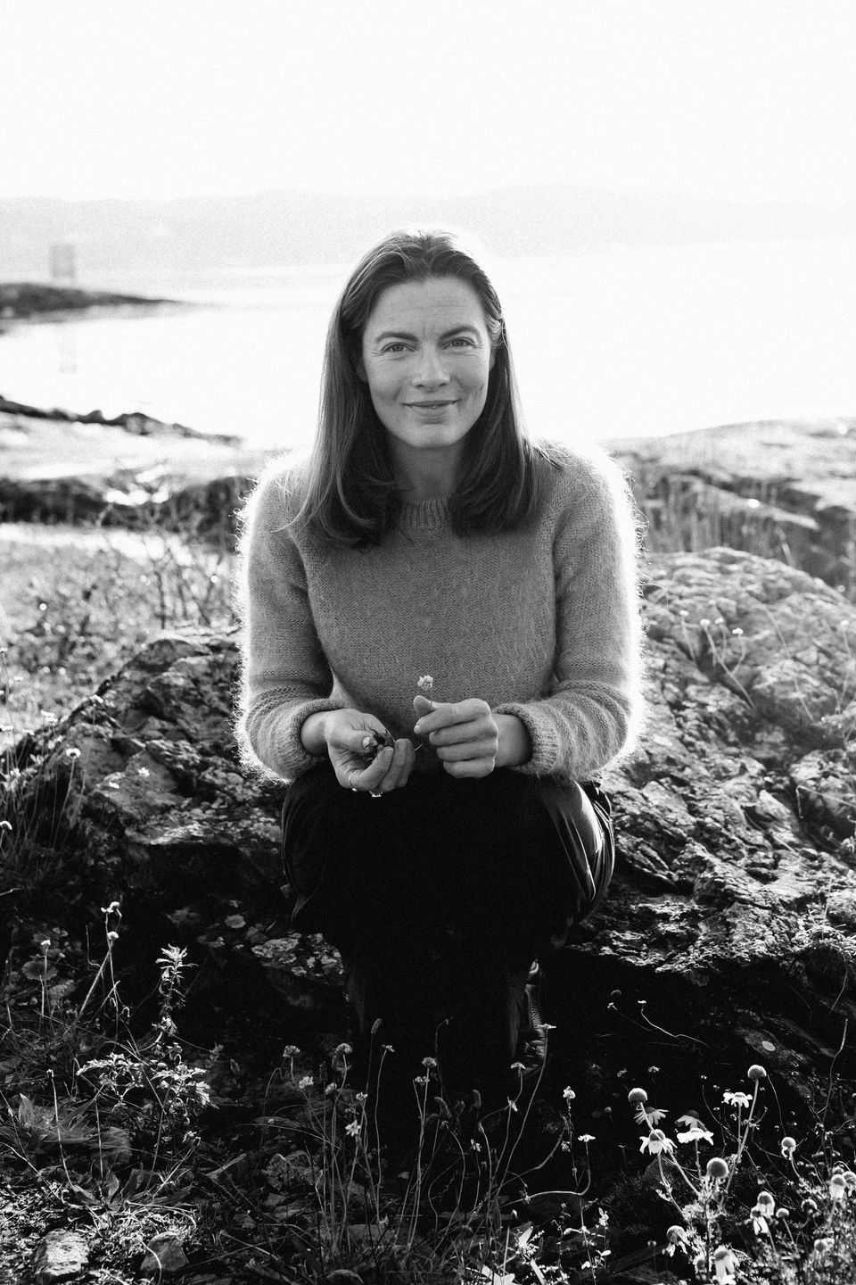 Marthe Magerøy sitter på et svaberg ved sjøen i ullgenser, svart-hvitt