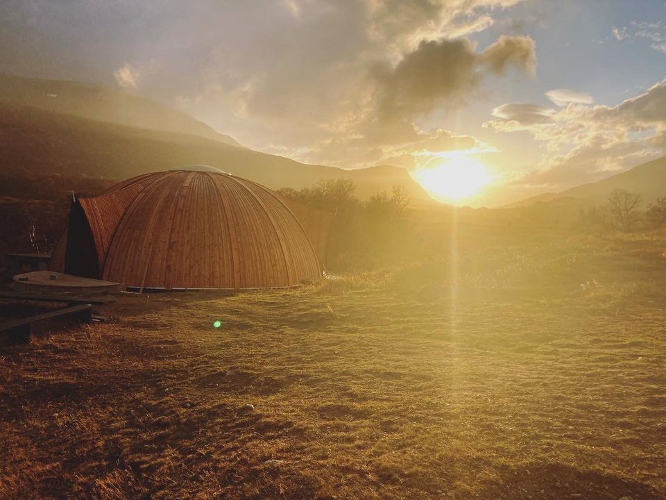 En kuppel av tre i fjellandskap i solnedgang