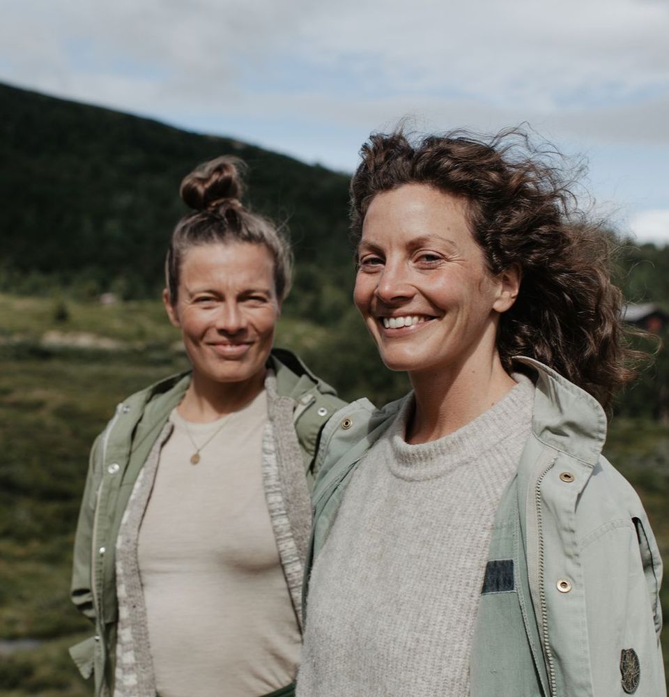 Marthe og Torunn smiler i vinden, med grønne jakker og fjell bak